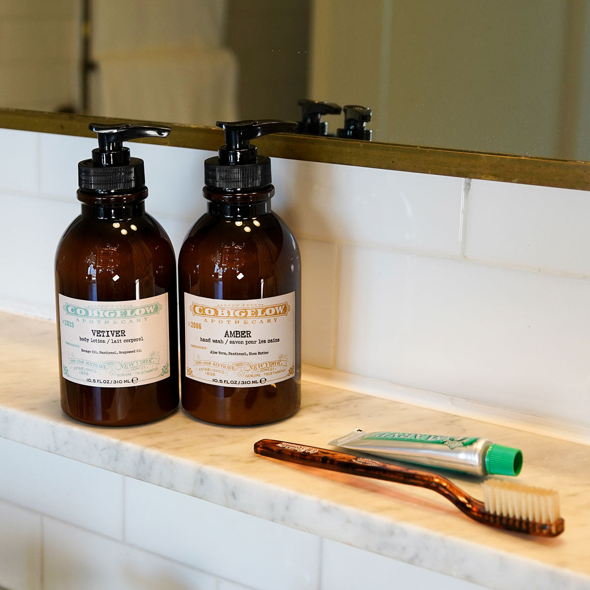 C.O. Bigelow Iconic Collection Vetiver Body Lotion and Amber Hand Wash on a Bathroom counter next to C.O. Bigelow Tortoise toothbrush and Marvis toothpaste tube. 