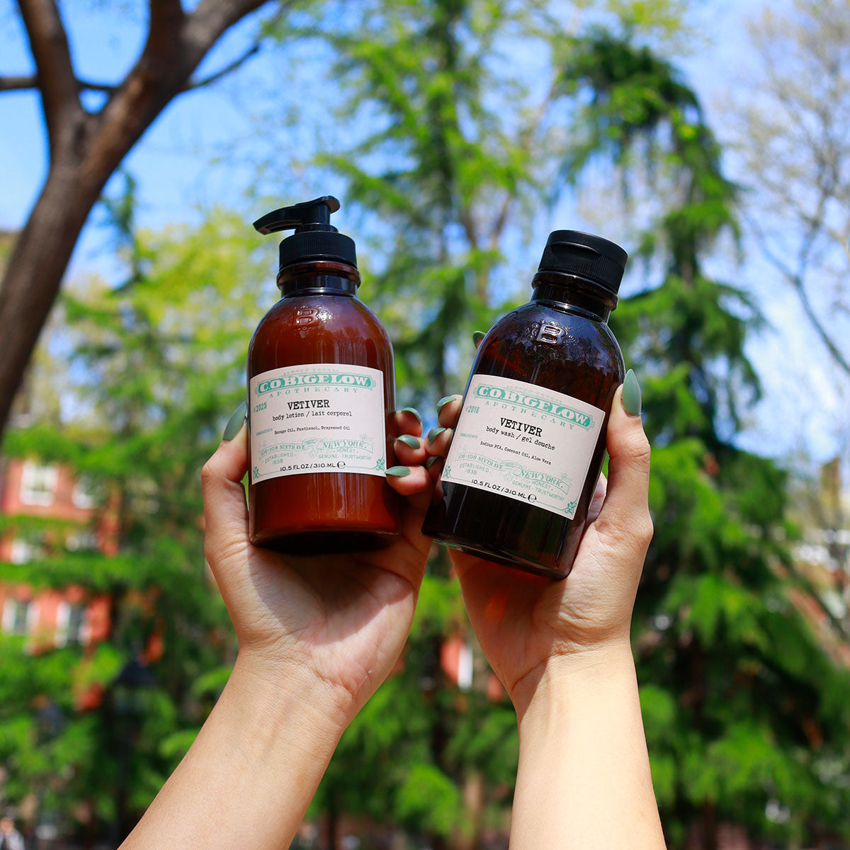 C.O. Bigelow Iconic Collection Vetiver Body Lotion and Body Wash held in persons hands in front of greenery. 