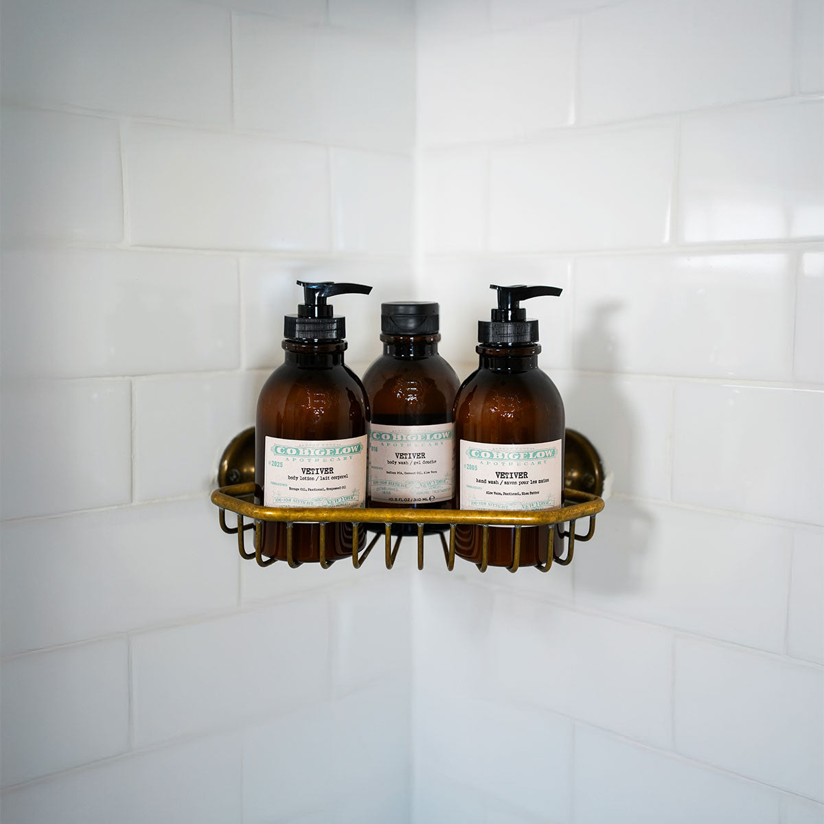 C.O. Bigelow Vetiver Body Lotion, Body Wash, and Hand Wash on a brass shelf in a bathroom shower. 
