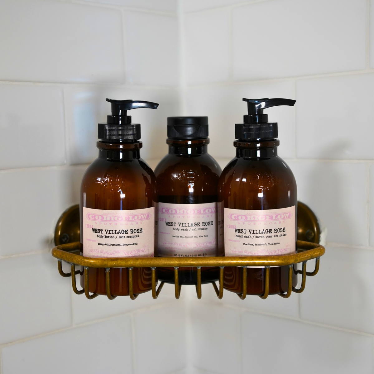 C.O. Bigelow West Village Rose Body Lotion, Body Wash, and Hand Wash on a brass shelf in a bathroom shower. 