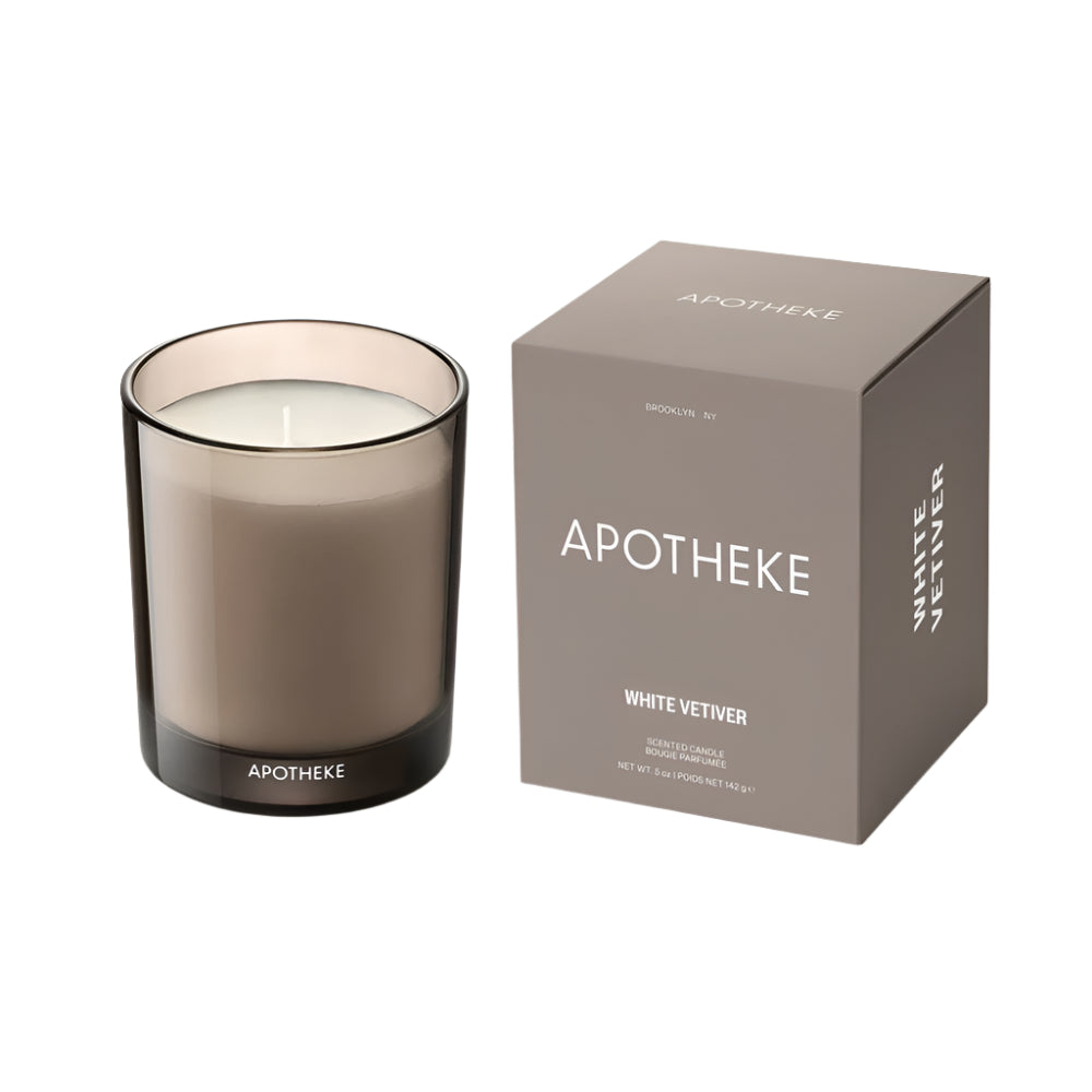 Apotheke White Vetiver scented candle in a clear glass jar with a gray lid, alongside its packaging box with 'APOTHEKE' and 'WHITE VETIVER' printed on it.