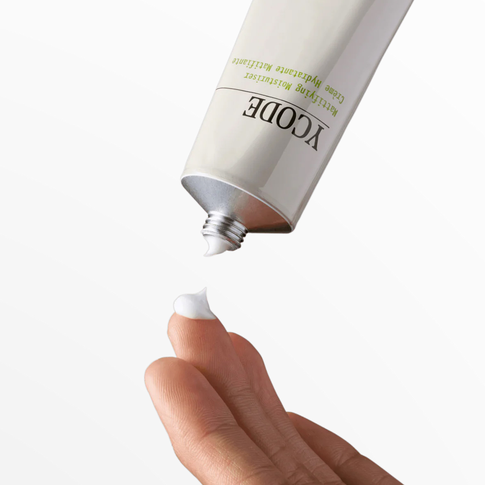 Hand applying white cream from a tube on a white background.