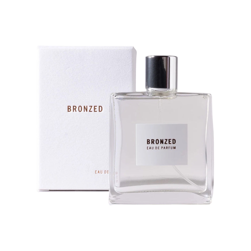 A clear glass bottle of Bronzed Eau de Parfum with a white label, next to its white box packaging with the brand name 'Bronzed' and product name 'Eau de Parfum' visible.