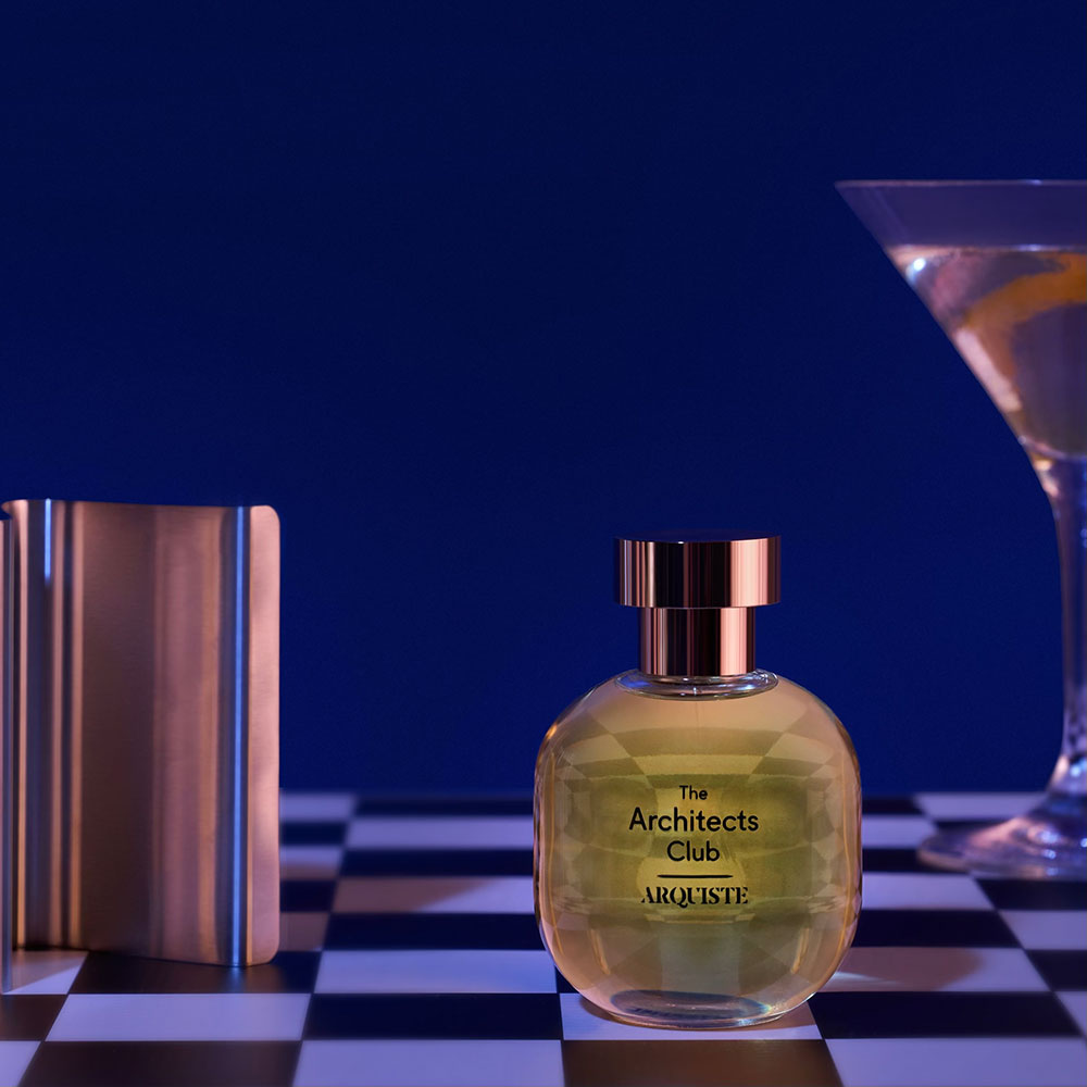 A bottle of 'The Architects Club' eau de parfum by Arquiste on a checkered background next to a glass with a drink inside