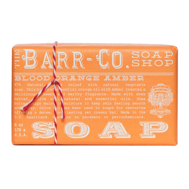 A rectangular bar of soap with orange packaging, labeled 'BLOOD ORANGE AMBER'. The soap is tied with a red and white string and has product information printed on it.