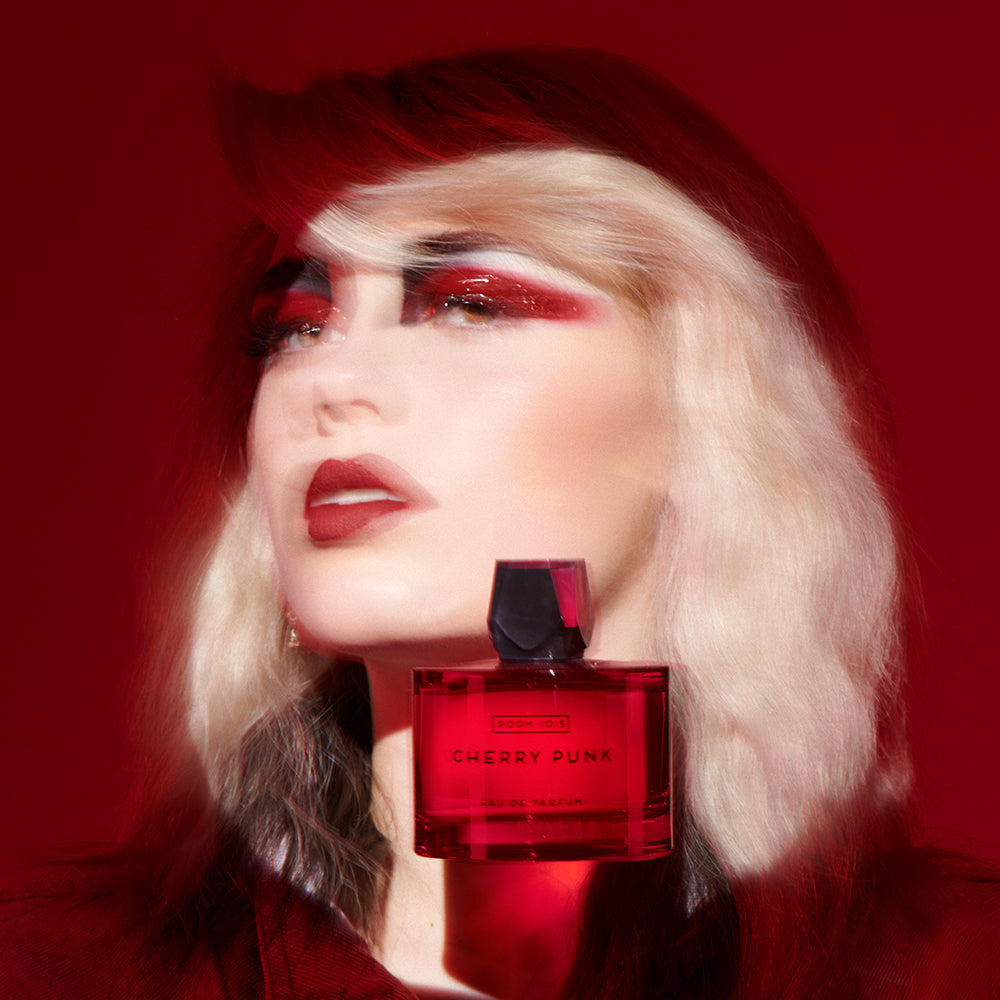 Cherry Punk - Eau de Parfum bottle floating by a blurred woman's spotlit face on a red background