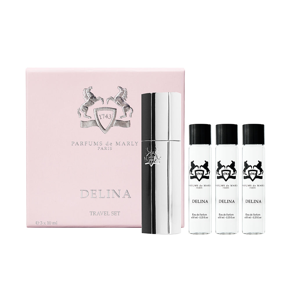 The image shows the Delina Travel Set by Parfums de Marly, which includes a refillable travel spray and three refill vials, packaged in a pink box with the brand and product name.