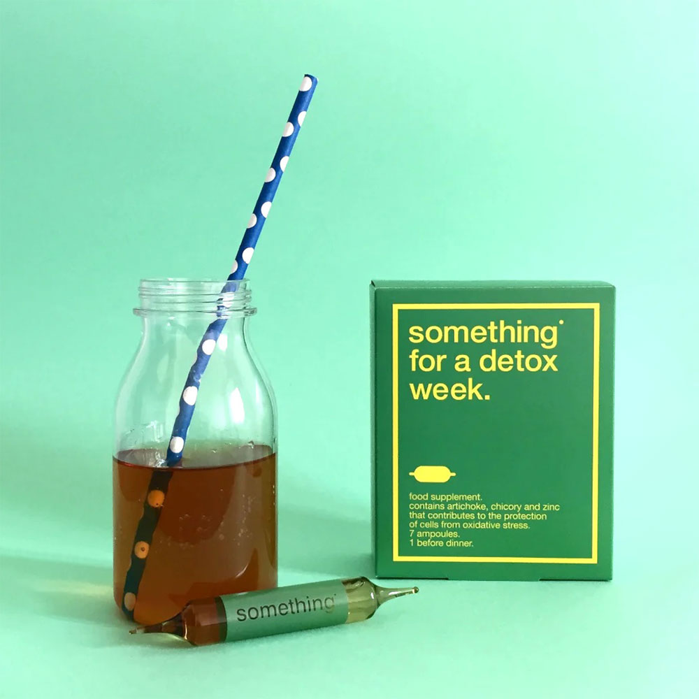 Box of something for a detox week next to a brown beverage on a green background