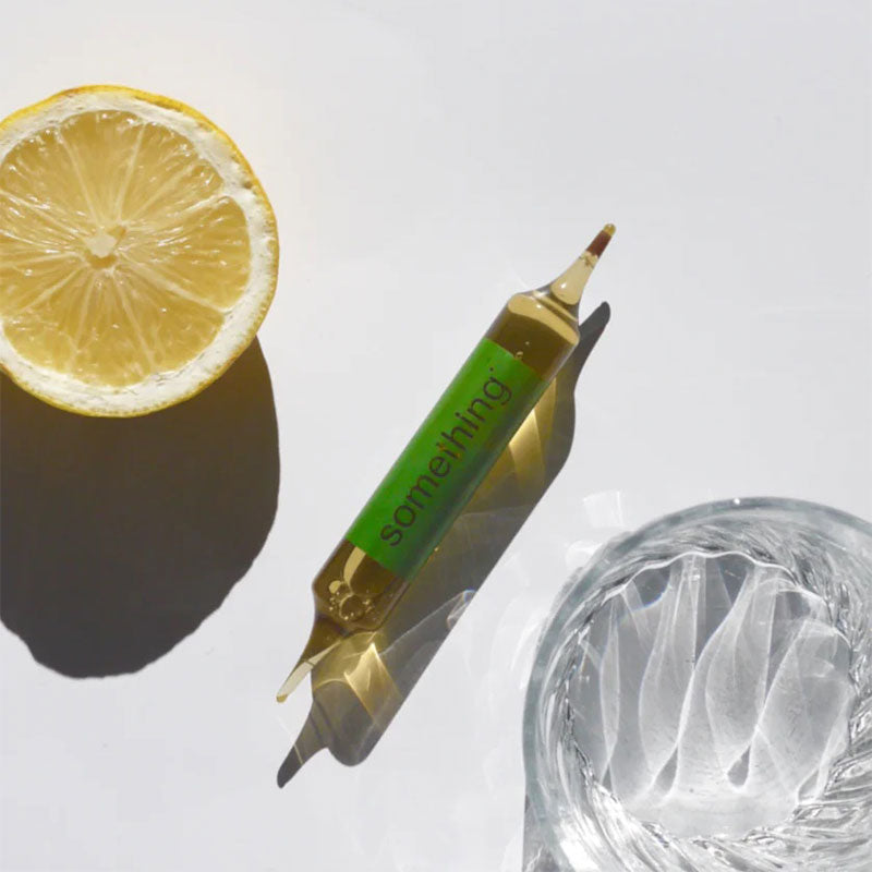 Ampoule with a green label next to a lemon and a glass of water