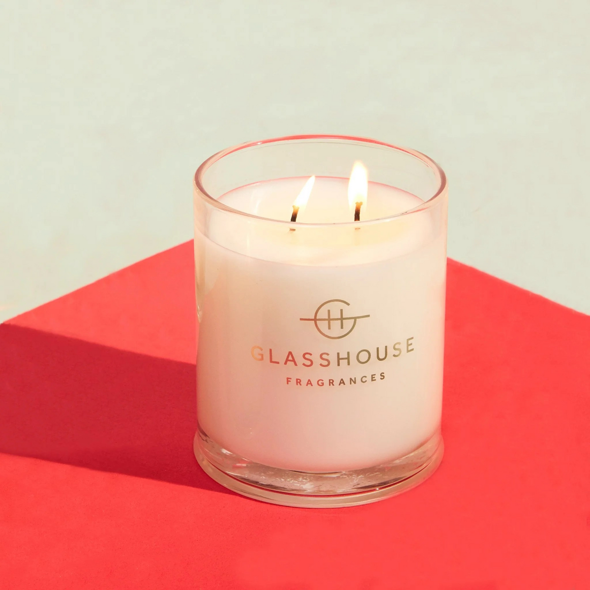 Glasshouse Fragrances Midnight in Milan Candle with both wicks burning on a pinkish table top with white background.