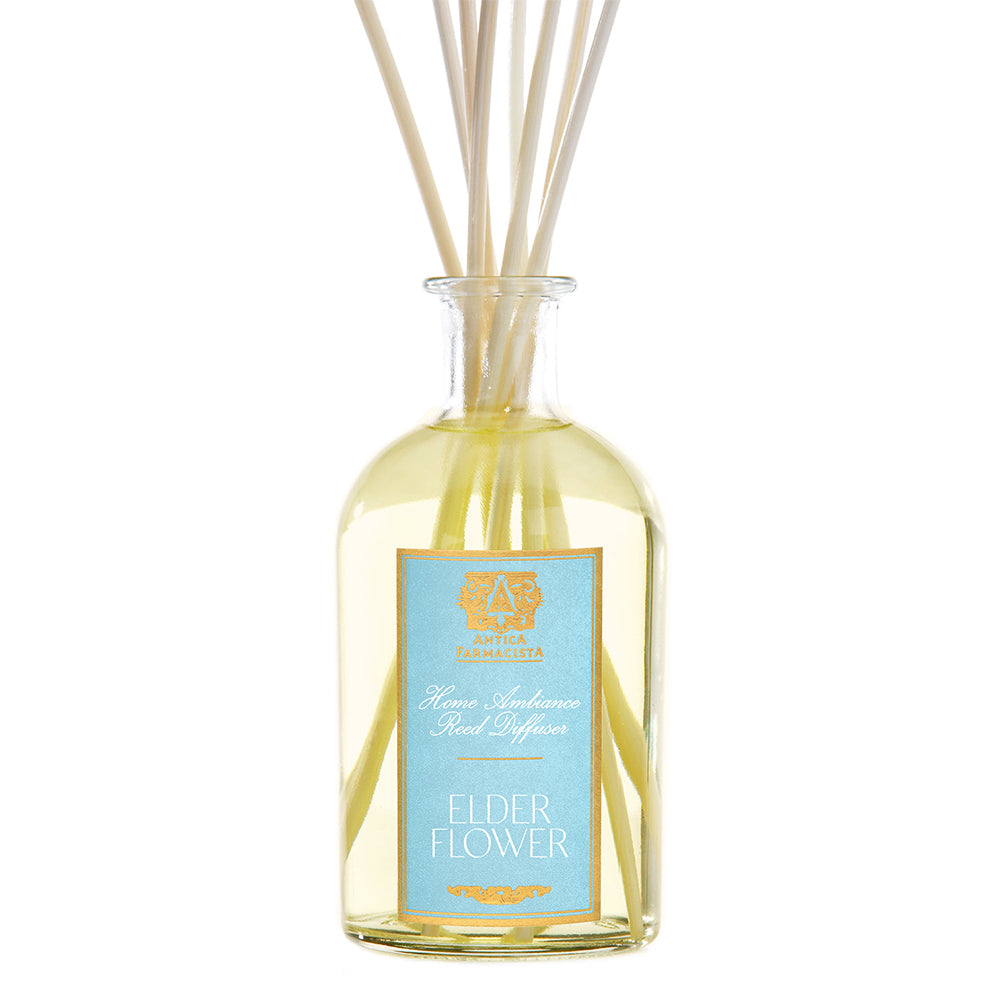 A clear glass diffuser bottle with a yellow liquid and white reeds inside, labeled 'Elderflower'.