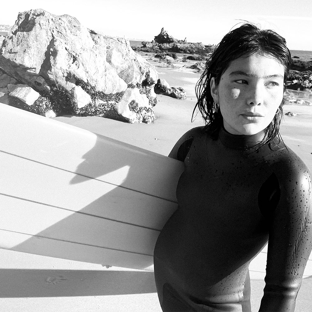 Woman in wetsuit with surfboard on a rocky beach