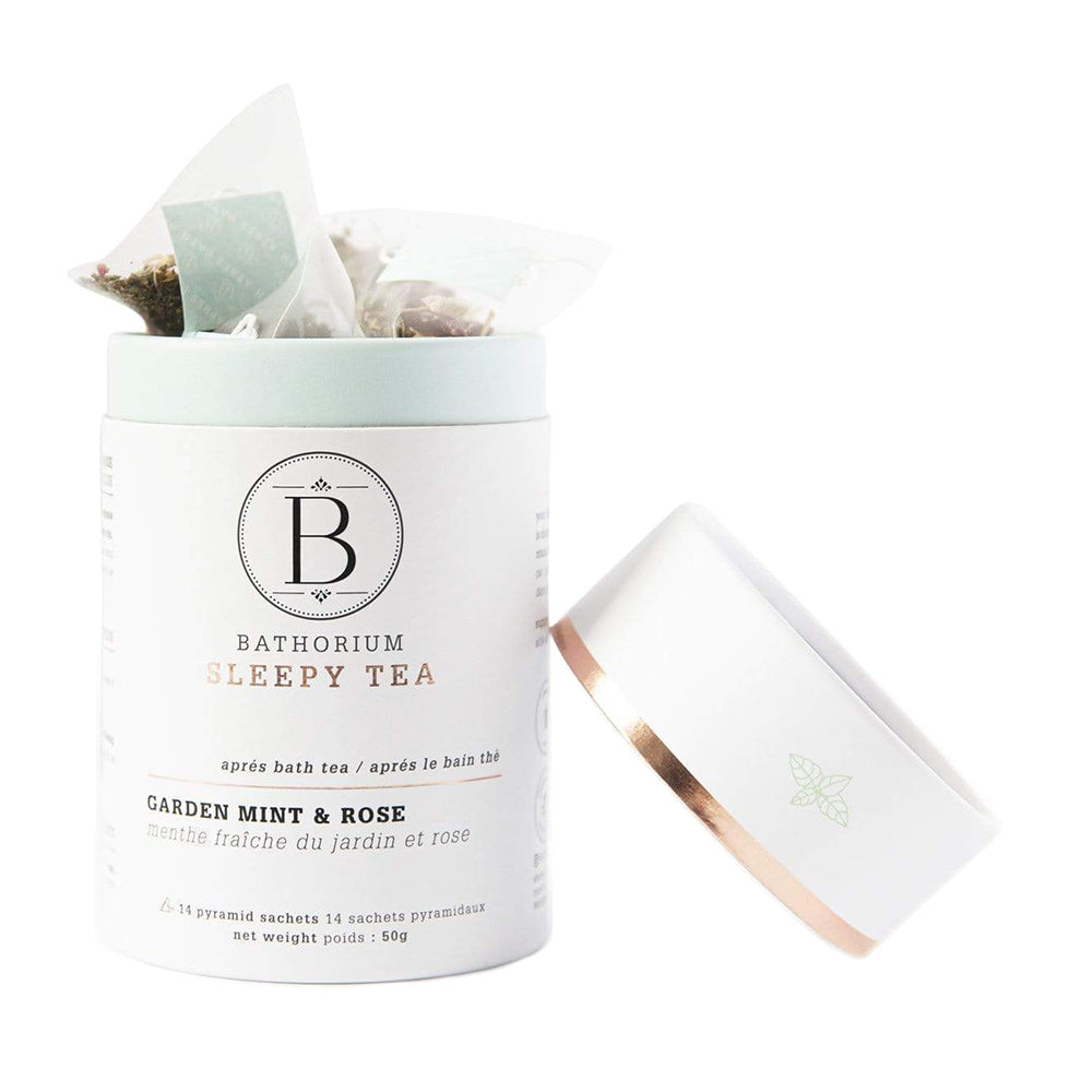 A white cylindrical tin with a rose gold lid labeled 'BATHORIUM SLEEPY TIME TEA GARDEN MINT & ROSE' containing pyramid tea bags visible through the transparent section of the lid.