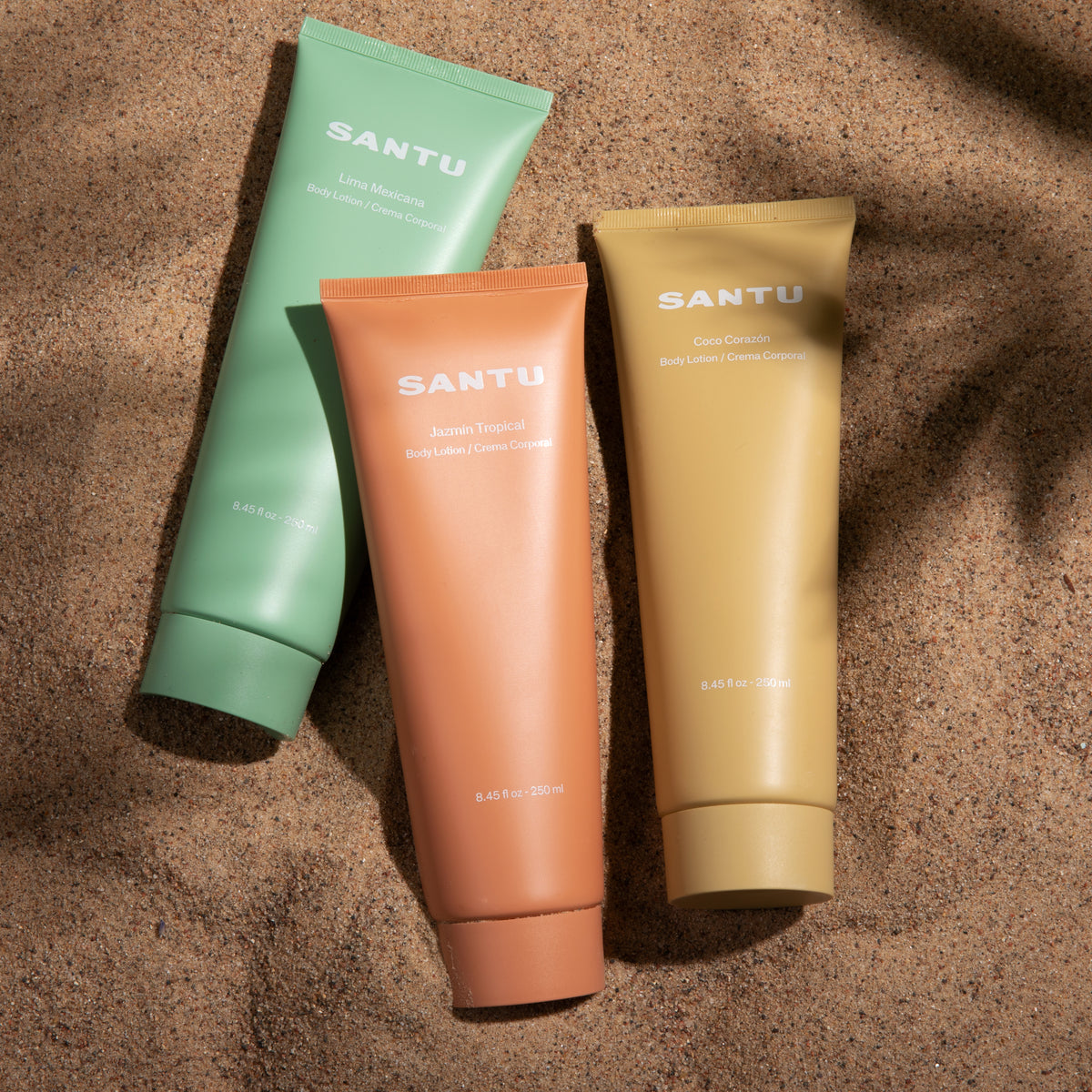 Three Santu body lotion bottles in green, orange, and coral on a textured brown surface.