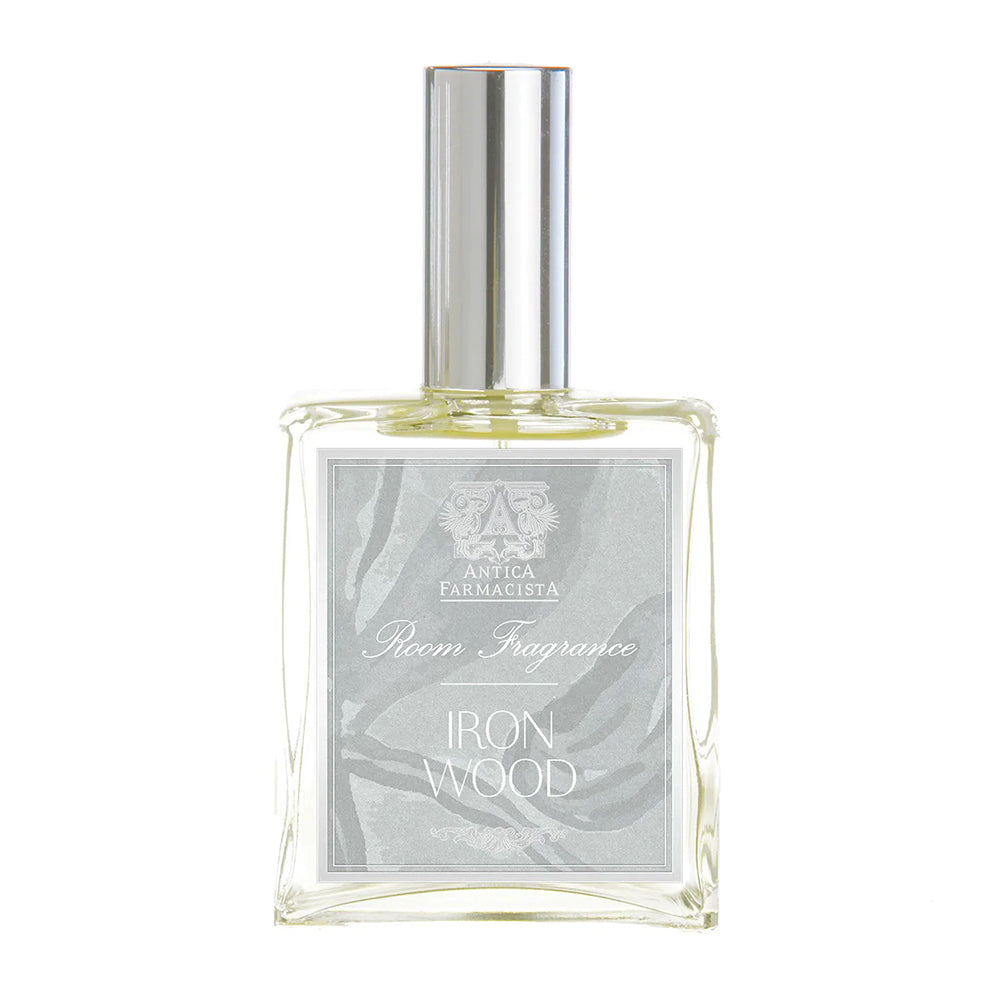 A clear glass bottle of Antica Farmacista Room Fragrance with a silver cap, labeled 'Iron wood'.