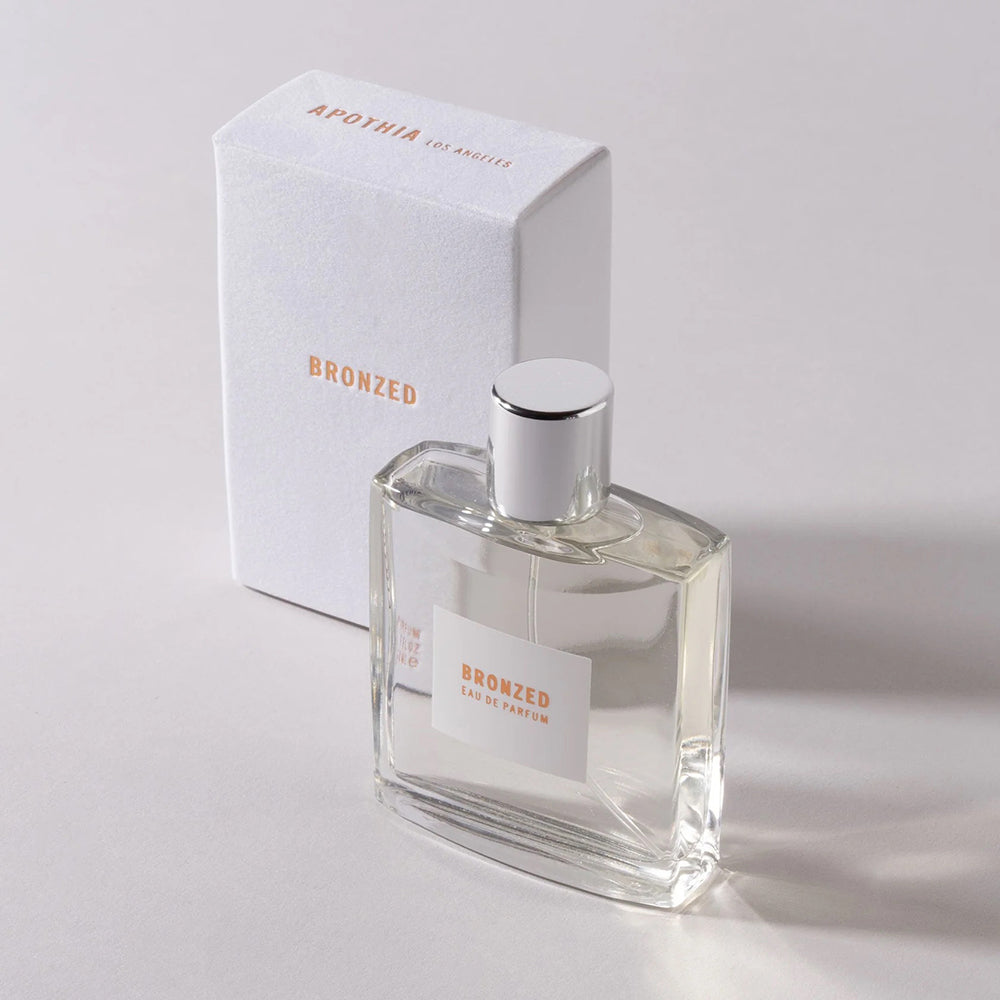 Bronzed perfume next to its packaging in front of a white background