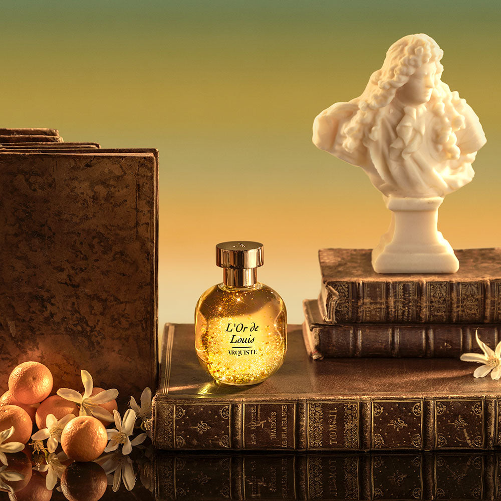 A bottle of L'Or de Louis Eau de Parfum by Arquiste on top of books next to a small marble statue