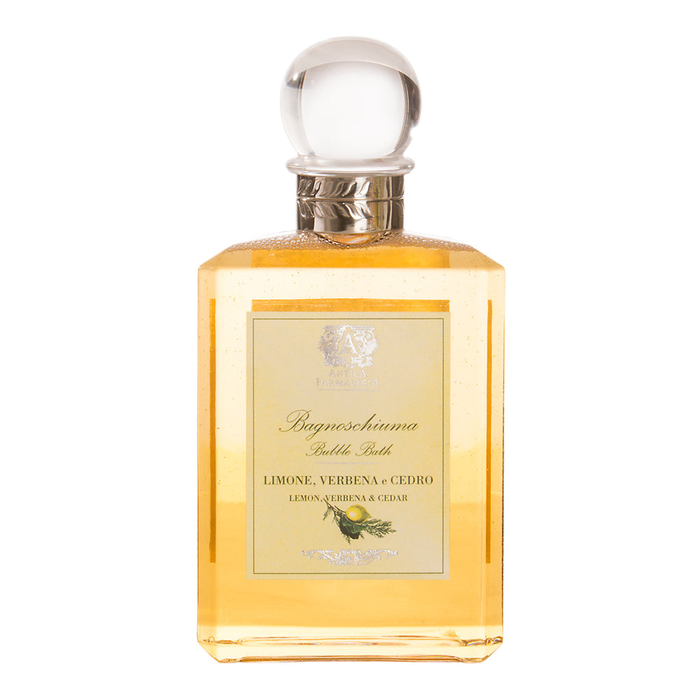 A bottle of Antica Farmacista Bubble Bath in a yellow-gold hue with a label that reads 'LIMONE, VERBENA, CEDRO'. The bottle has a clear glass and a silver cap.