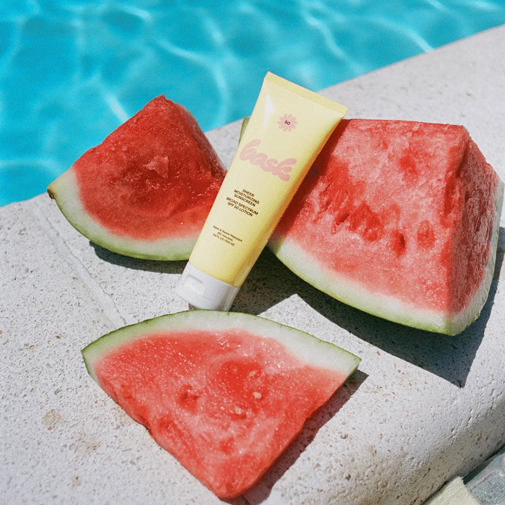 Bask sunscreen lotion on a pool side among pieces of watermelon
