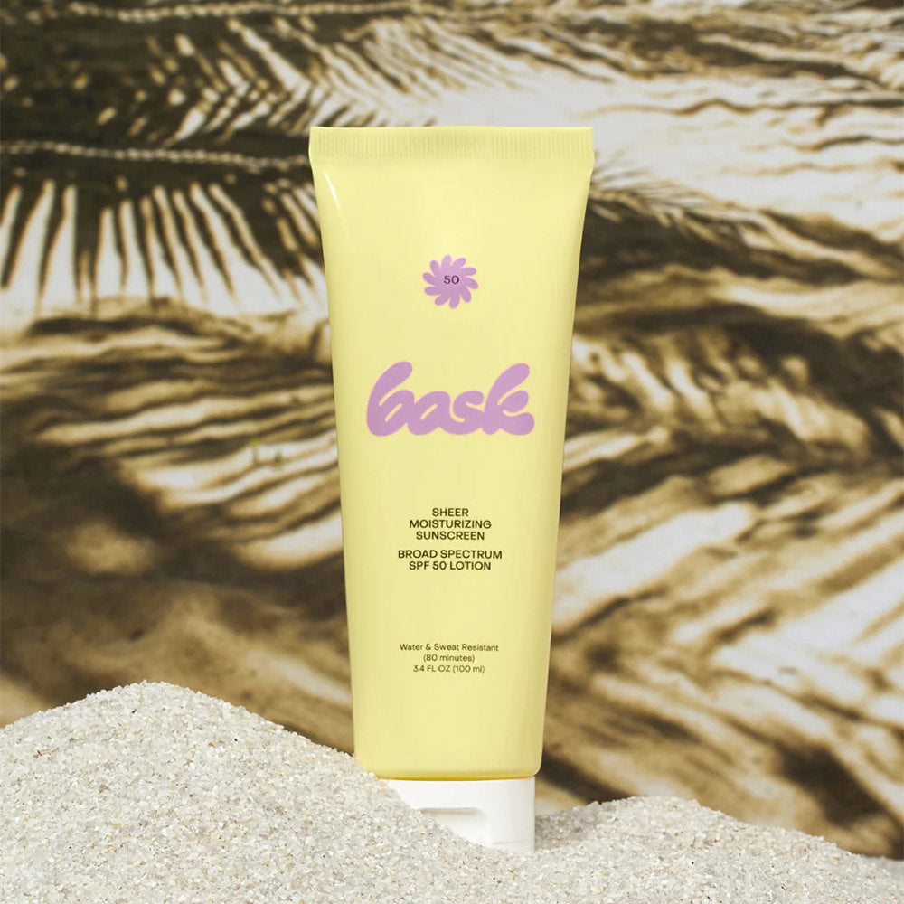 Bask sunscreen lotion on a sandy surface with palm trees in the background