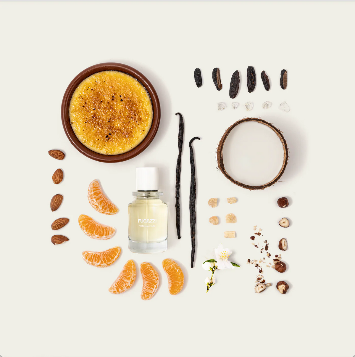 fugazzi vanilla haze perfume bottle with vanilla beans, nuts and citrus slices and a creme brulee around it. 