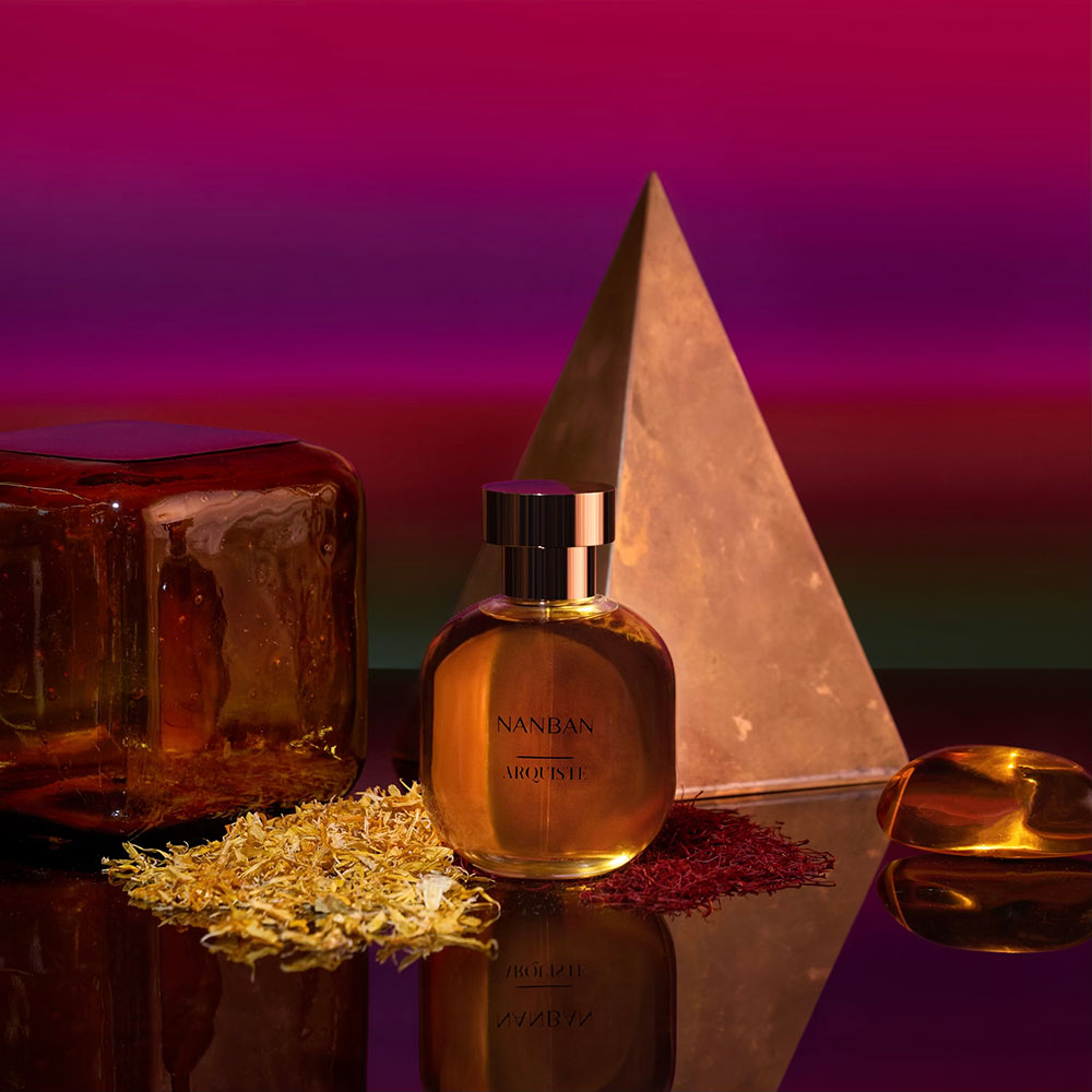 A bottle of NANBAN Eau de Parfum in front of a small pyramid shape and unidentifiable clear objects.