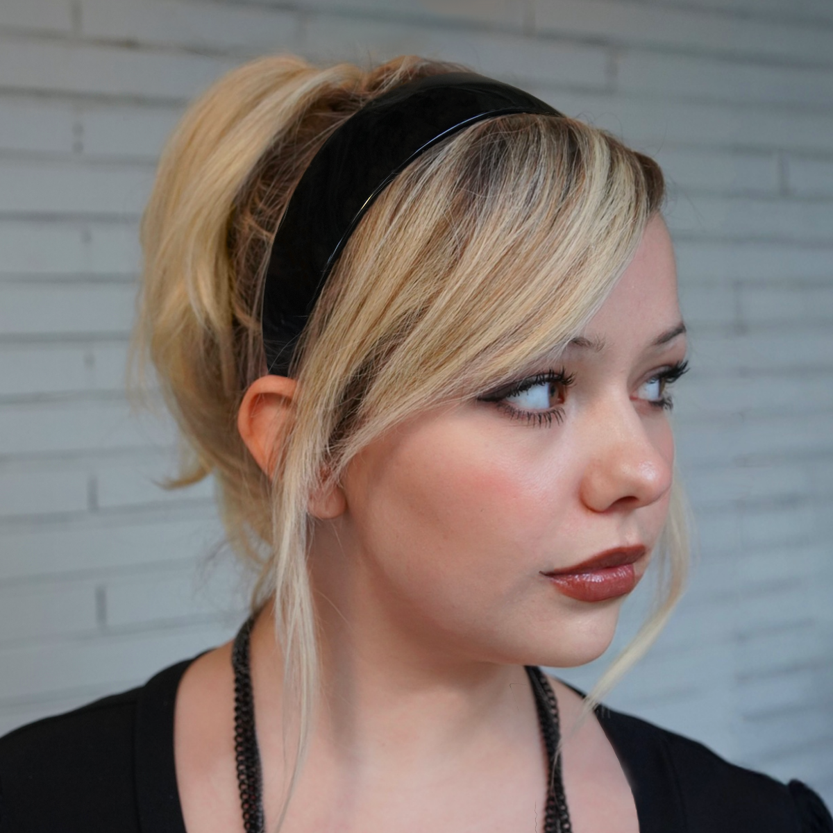 Woman modeling a black C.O. Bigelow Charles Wahba 1.5 inch headband in front of a brick wall. 