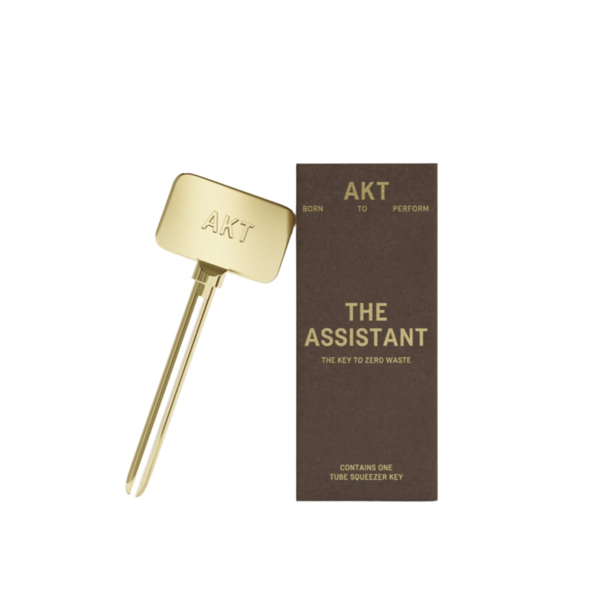 AKT's gold Assistant Tube Squeezer Key leaning on brown packaging box that reads "The Assistant."