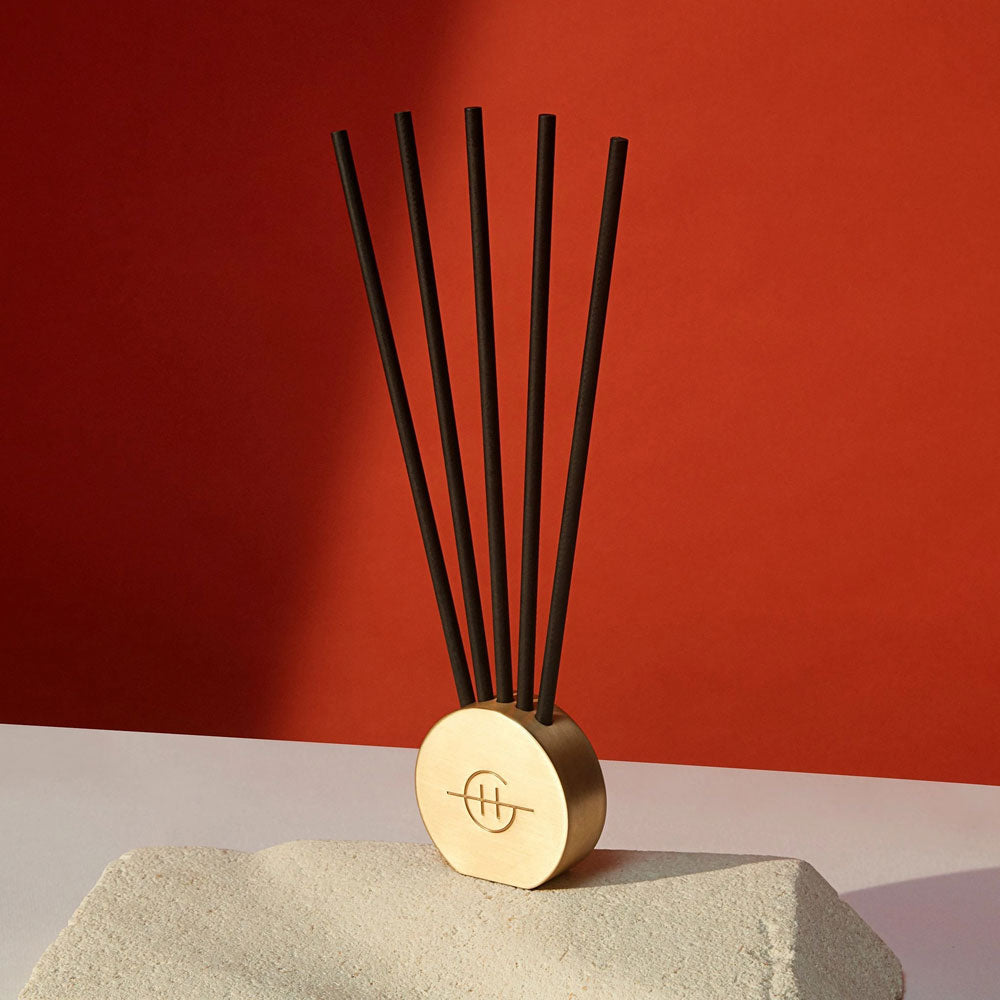 Glasshouse Fragrances Scent Stone Metal Vessel.  Gold circular vessel shown with scented sticks against a red wall.