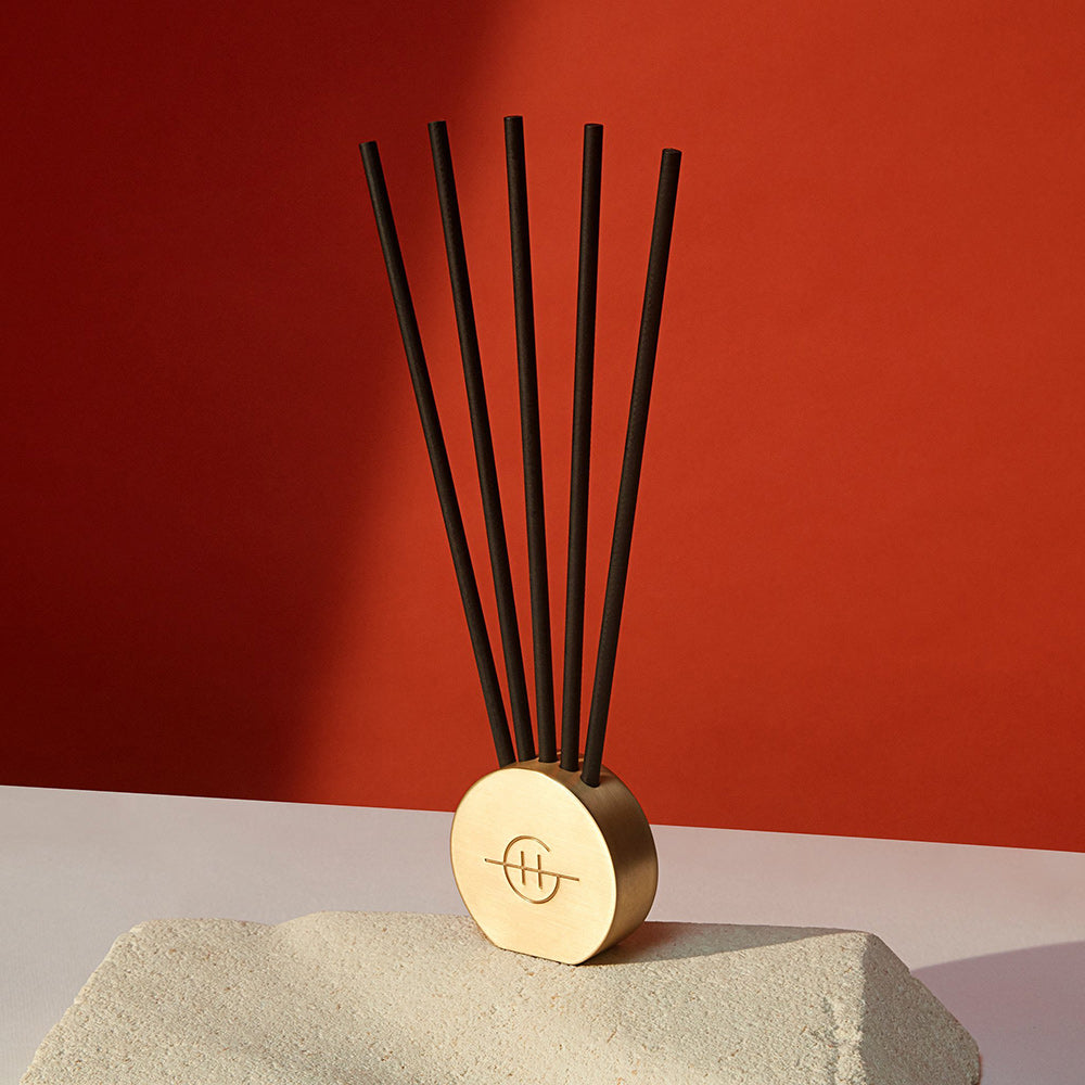 Glasshouse Fragrances Scent Stone Metal Vessel.  Gold circular vessel shown with scented sticks against a red wall.