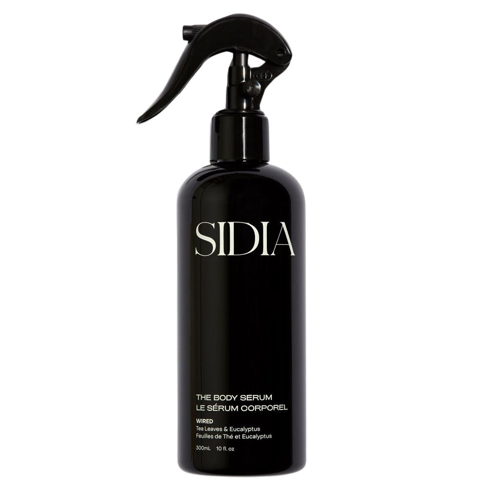A black spray bottle labeled 'SIDIA' with 'THE BODY SERUM LE SERUM COMPARTMENT' and 'Pour une peau hydrate' printed on it, indicating it is a plant-based body serum.