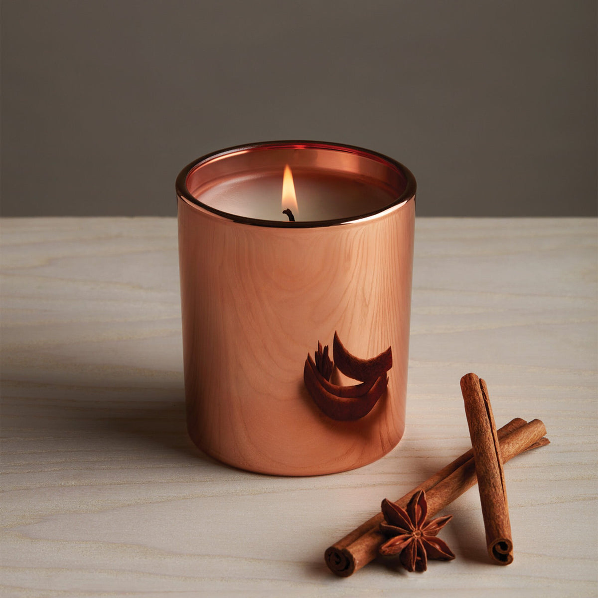 Copper candle with cinnamon sticks and star anise on a wooden surface