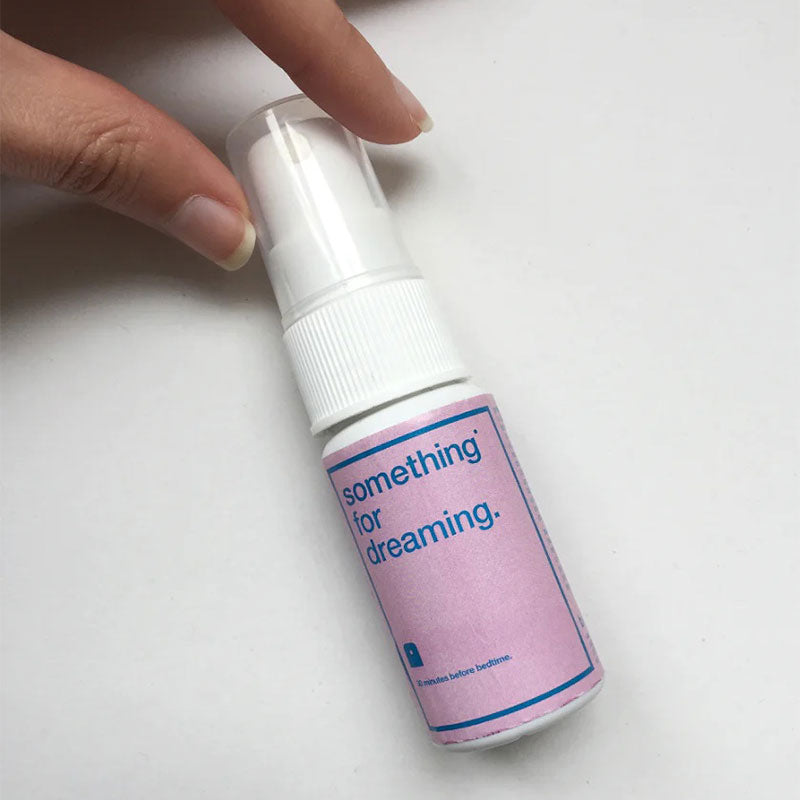 Hand holding a spray bottle with a pink and blue label with the words "something for dreaming"