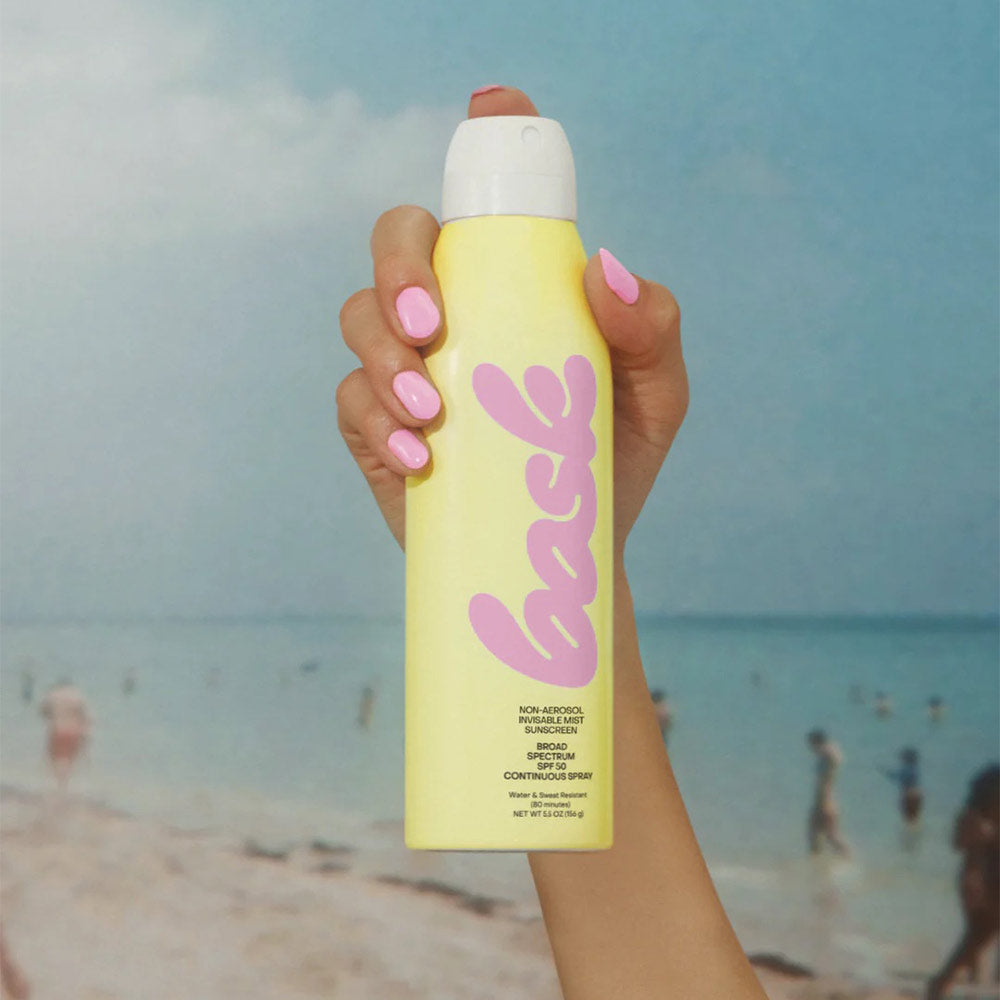 Hand holding bask sunscreen in front of a beach setting