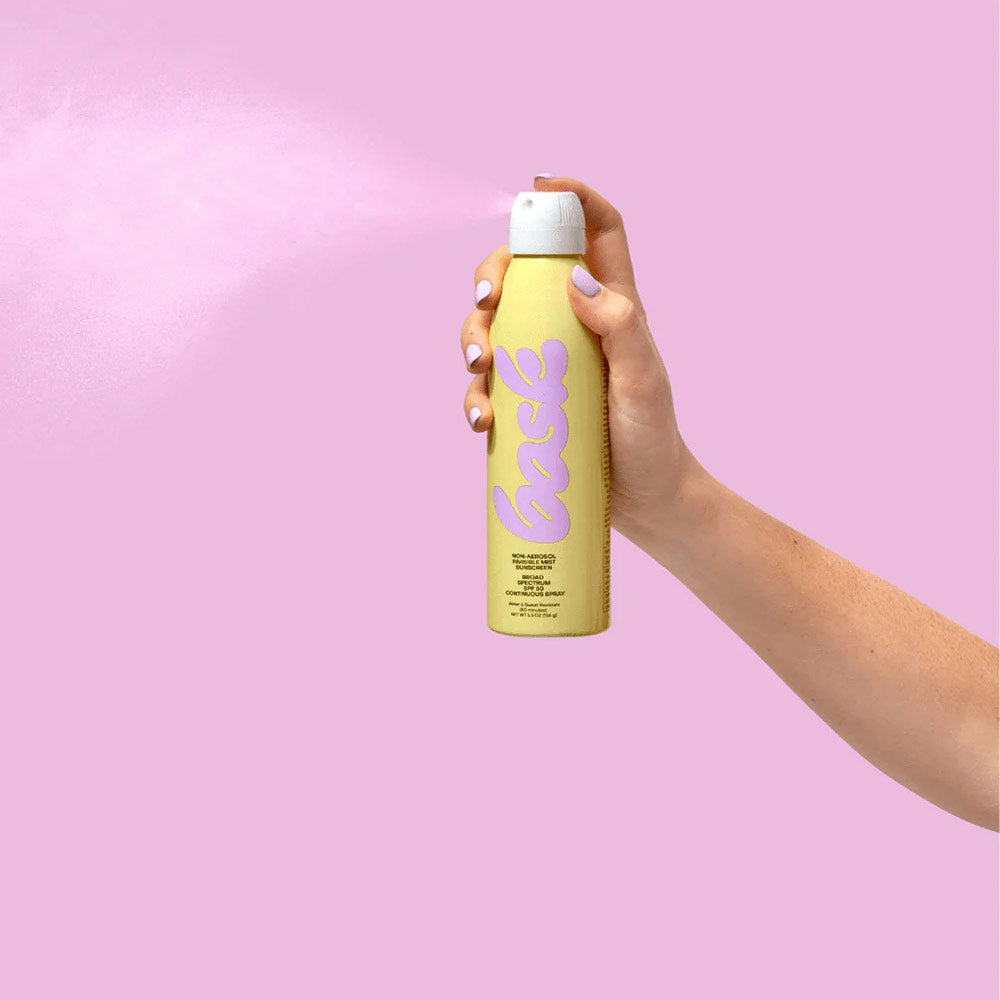 Hand spraying Bask sunscreen on a pink/purple background