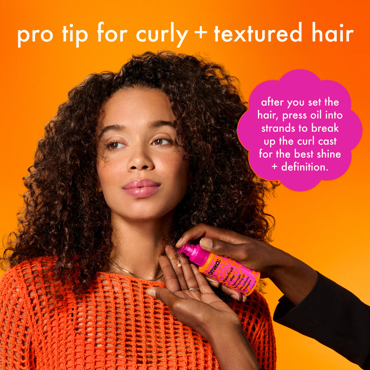 Woman with curly hair holding a bottle of  Amika Superfruit Star against an orange background